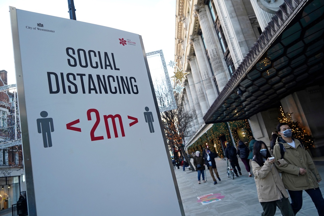  12月20日，在英国伦敦，行人走过牛津街上提醒人们保持社交距离的标牌。新华社 图