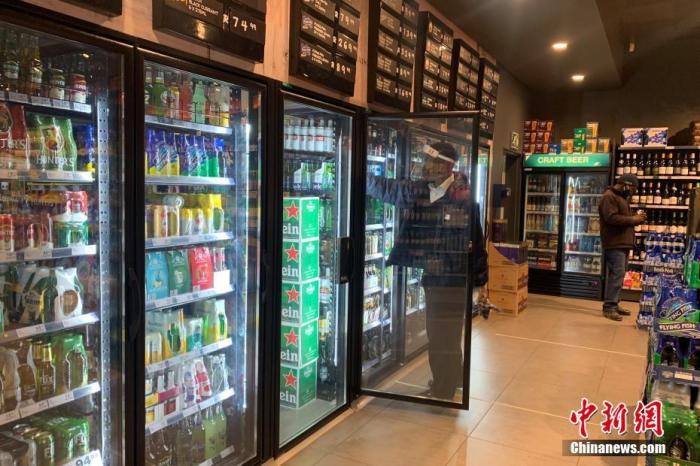 资料图:南非约翰内斯堡,一家酒类商店的店员佩戴面罩整理冰箱内的货物。 中新社记者 王曦 摄