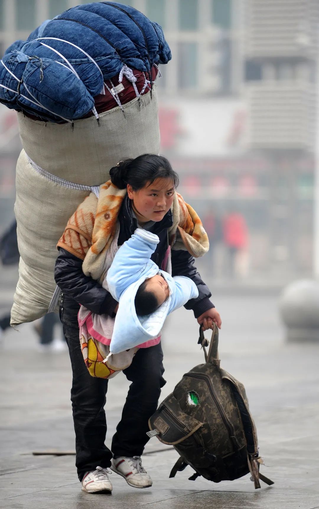 2010年1月30日，巴木玉布木背着大包、抱着孩子在南昌火车站匆忙赶车。周科摄