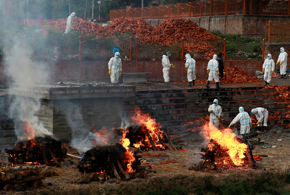 当地时间2021年5月5日，尼泊尔加德满都，穿着防护服的工作人员在露天火葬场上火化新冠死难者遗体。澎湃影像 图