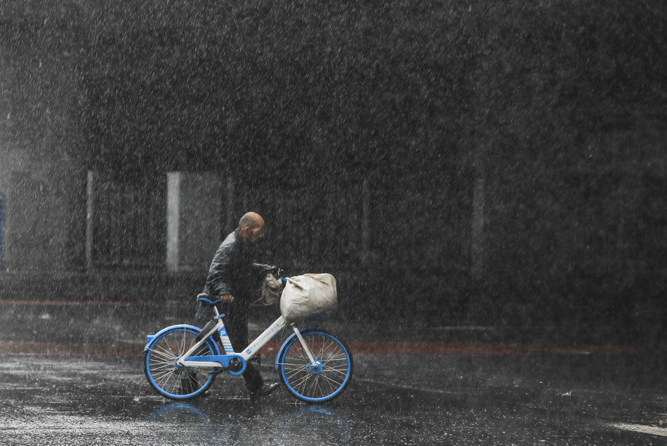 推着单车的市民在雨中行走