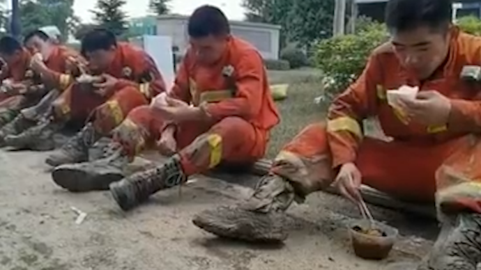河南郑州：消防员满身泥泞坐在地上吃午饭