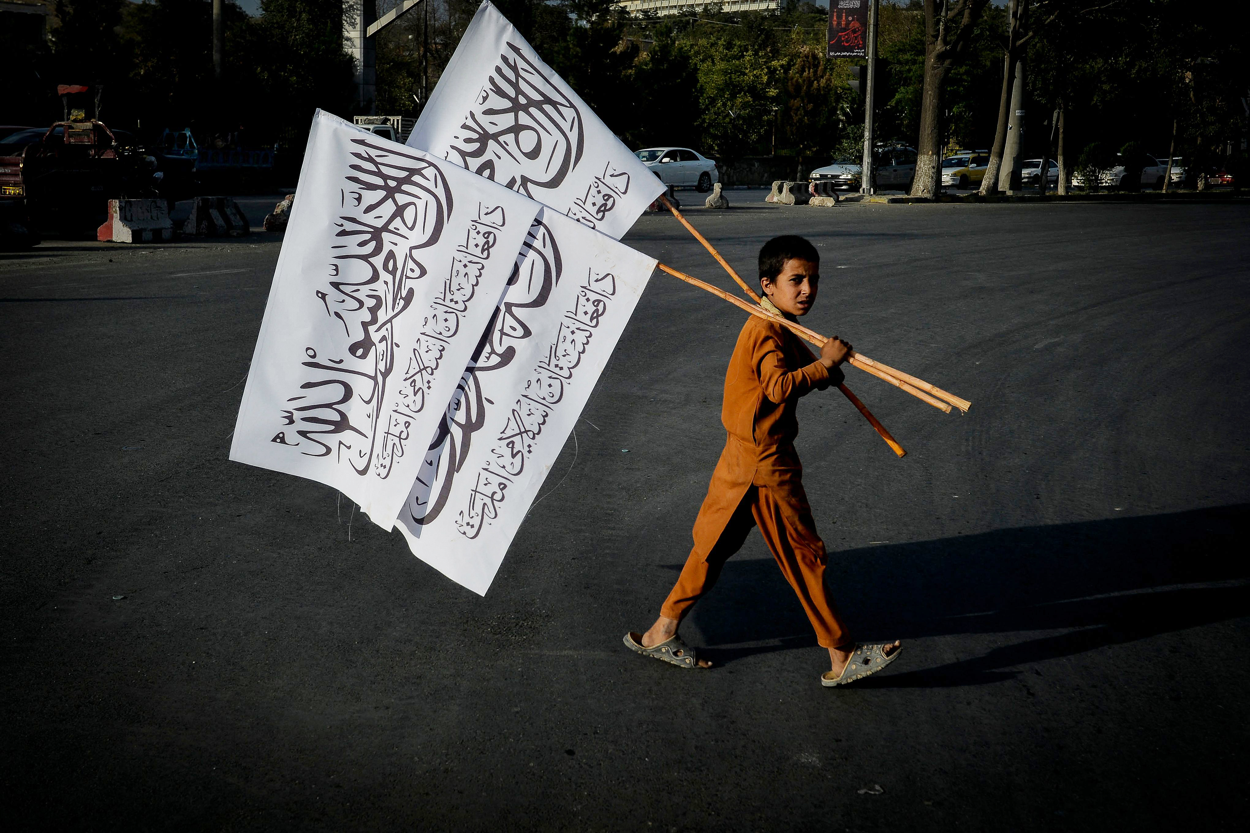 阿富汗首都喀布尔,一个小男孩扛着塔利班的旗帜走在街头