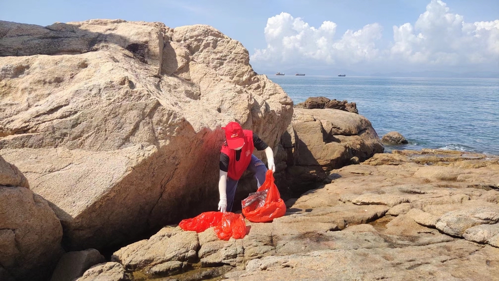 志愿者在沙灘礁石處清理垃圾。微信公眾號“愛大鵬” 圖
