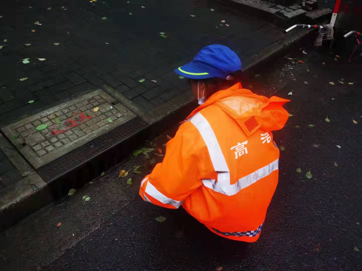 环卫工人清理道路排水口周边落叶、垃圾和淤泥。