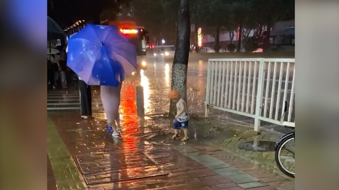 萌娃雨中踩水妈妈撑伞陪玩，爸爸拍视频记录