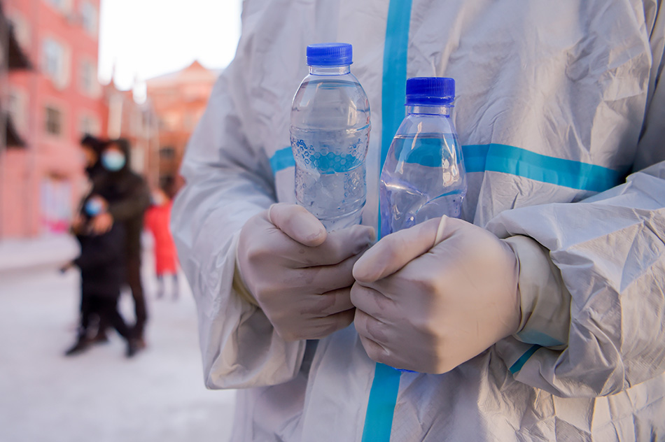 2021年12月1日，在内蒙古满洲里市聚友小区核酸采样点，工作人员用居民送的暖水瓶取暖。当日，内蒙古自治区满洲里市进行第四轮大规模核酸检测工作。李志鹏/新华社 图