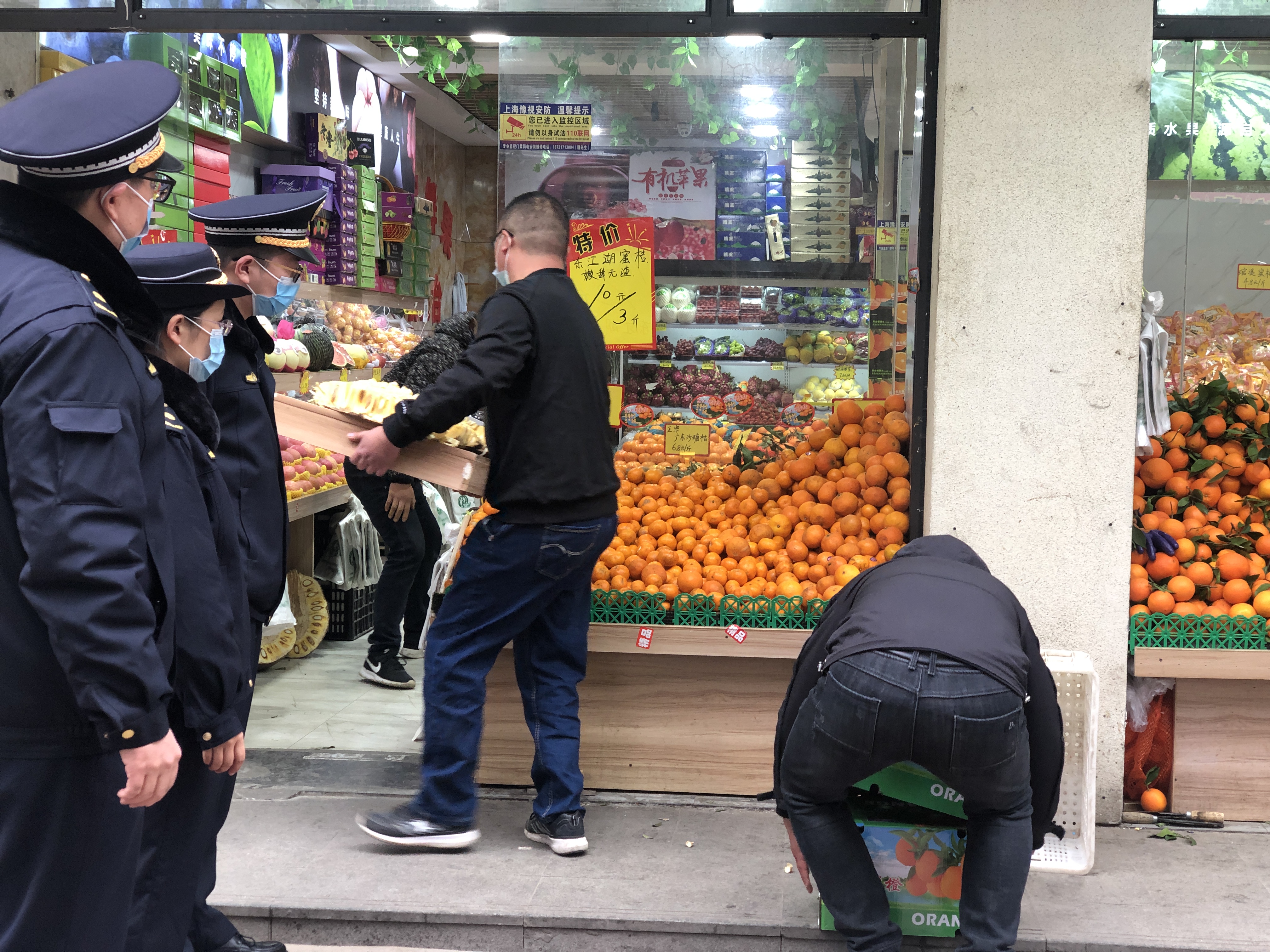 城管指导商贩将超出门窗陈设的水果搬进店内。