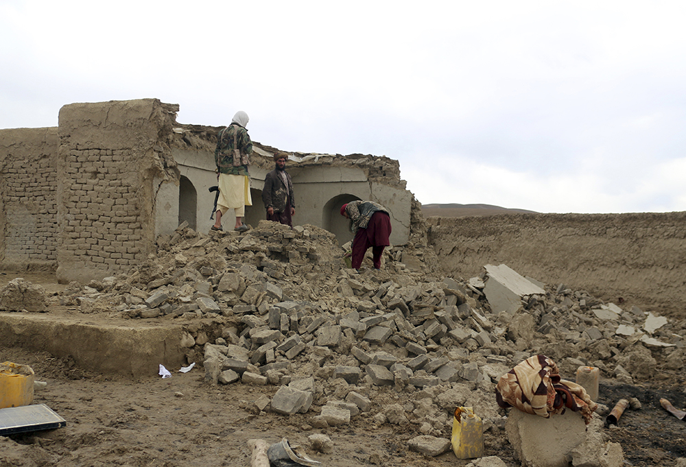 当地时间2022年1月18日，在阿富汗西部巴德吉斯省卡迪斯地区，当地居民站在房屋废墟中。