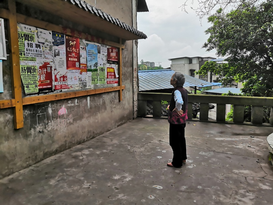 重庆水土镇一位老年人在贴满广告的墙前仔细看信息（相欣奕拍摄于2019年）