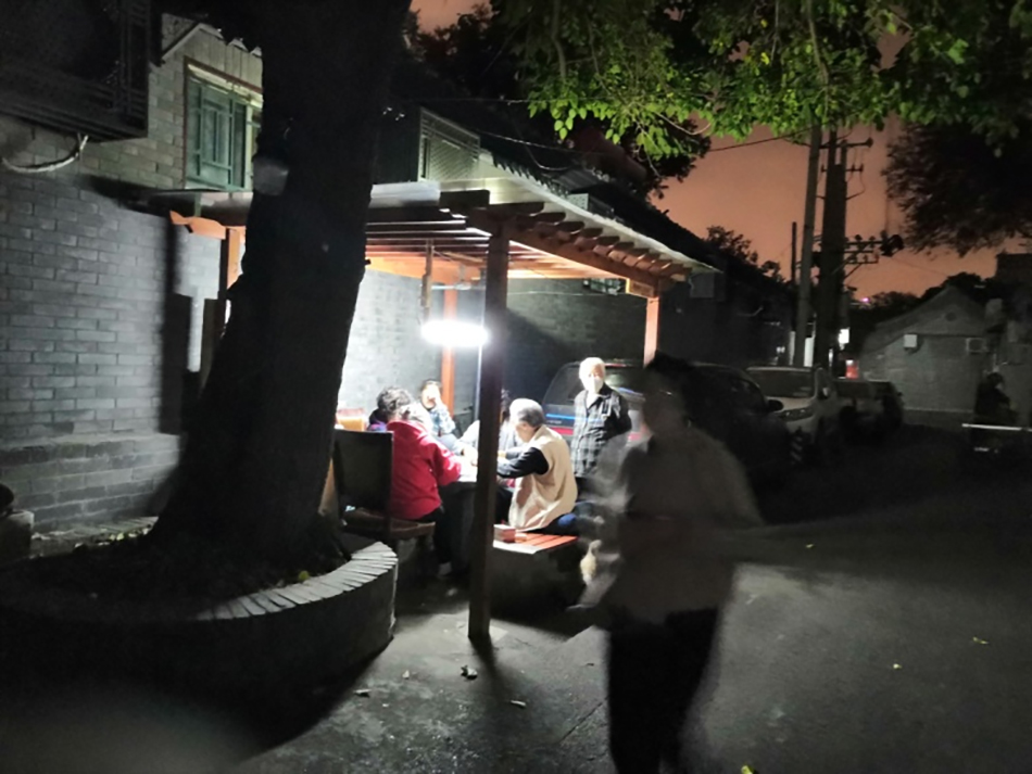 夜晚北京胡同中老年人在社区营造活动中搭建的木制简易亭灯光下打牌（相欣奕拍摄于2019年）