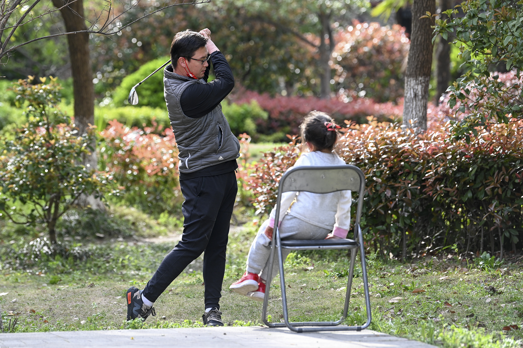 2022年3月28日，上海晶华坊，一位家长带着小孩在晒太阳，同时拿着高尔夫球杆进行挥杆练习。