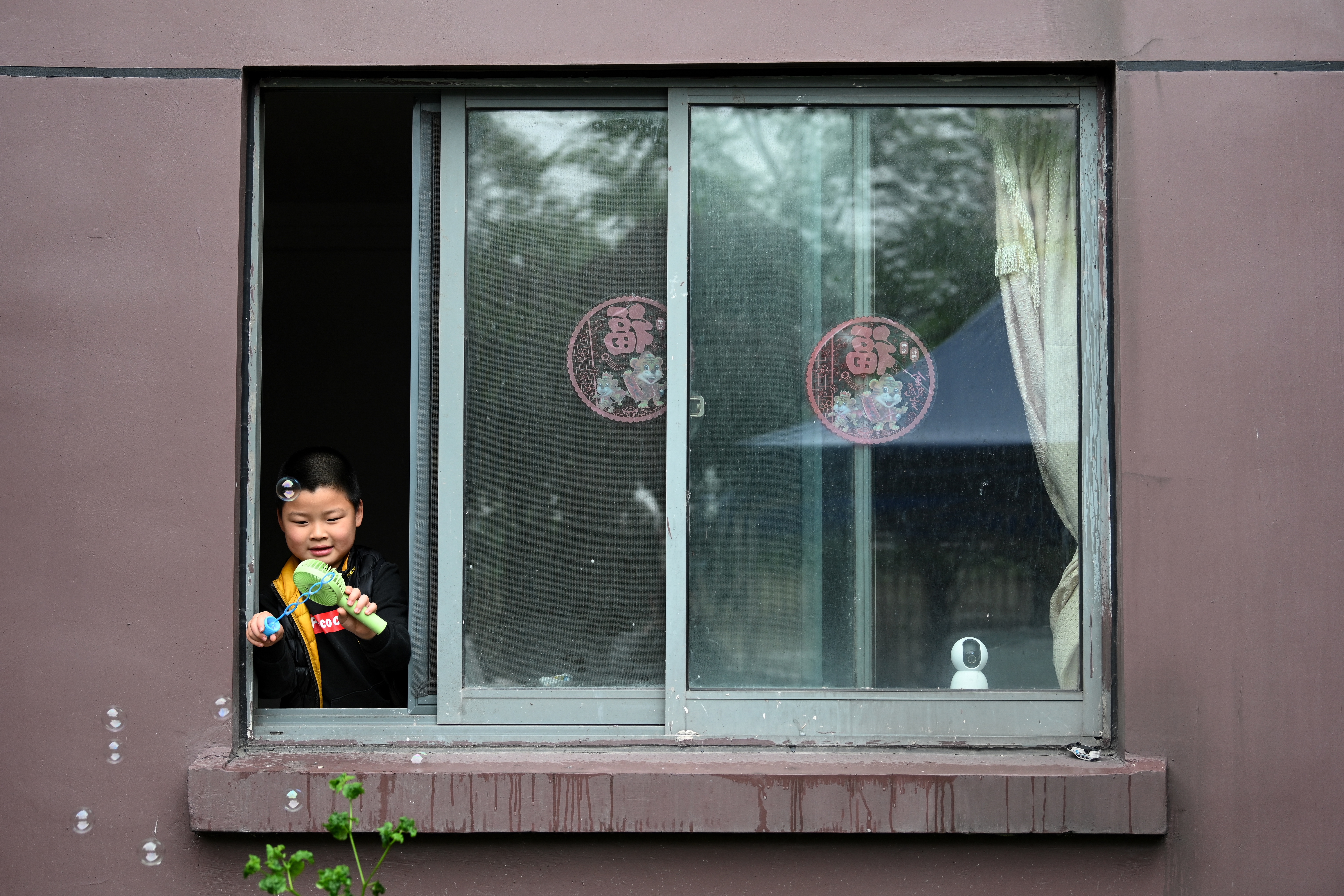 2022年5月13日,上海某小区,小男孩在窗边玩泡泡.