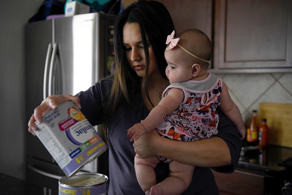 当地时间2022年5月19日，美国得克萨斯州休斯顿，全国婴幼儿配方奶粉持续短缺，Kim Anatra抱着她5个月大的女儿Sienna，她把罐子里最后的奶粉倒进最后一罐奶粉里。IC 图