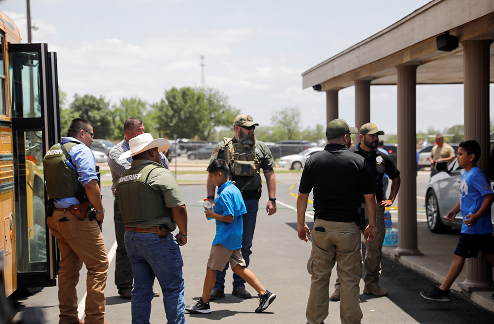当地时间2022年5月24日，美国得克萨斯州乌瓦尔德市，，一名儿童登上校车，执法人员守卫着枪击现场。