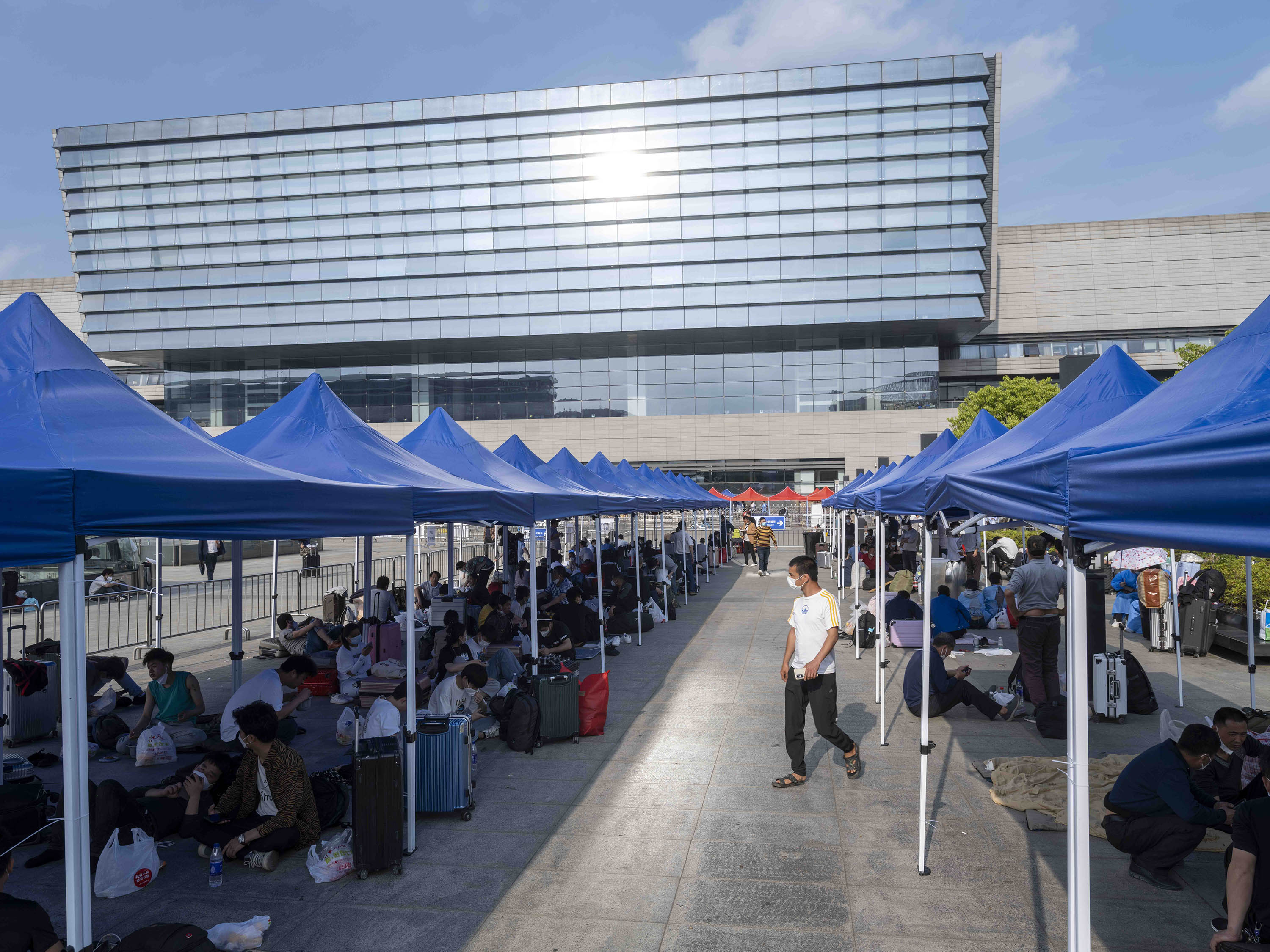 2022年5月26日，虹桥火车站前，人们在露天广场搭起的蓝色雨棚下休息。