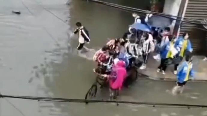 阿姨积水中骑三轮车来回载孩子们过马路