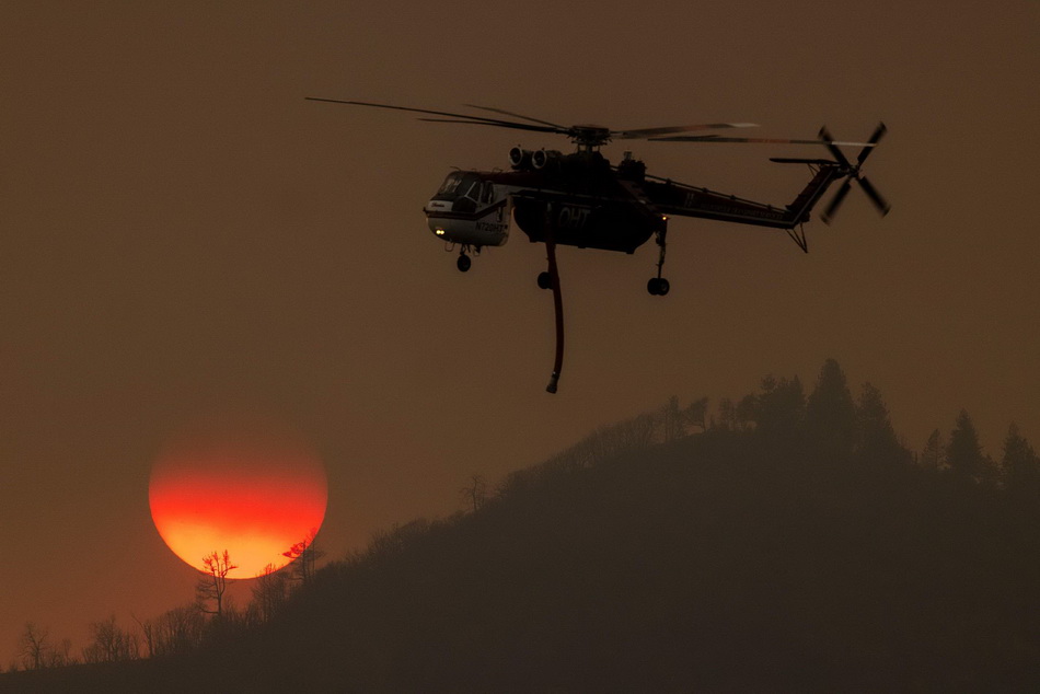 当地时间2022年7月24日，美国加州，一架消防直升机在扑灭橡树大火时飞过夕阳。VCG111393494465.jpg