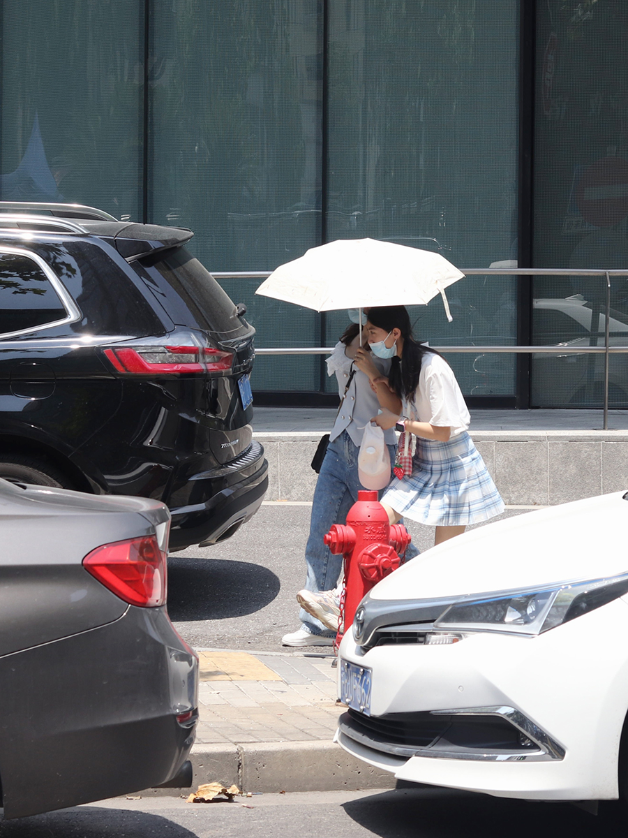 2022年8月15日，上海，汉中路地铁口，两名女子在烈日下共同打一把伞。实习生 刘心语 图