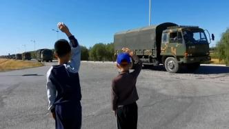 两名男孩向路过军车车队敬礼，车辆鸣笛回应