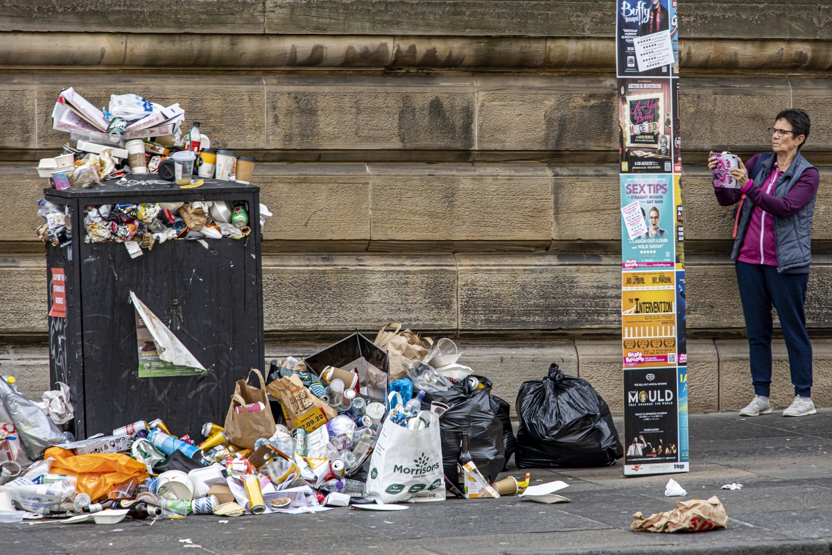 当地时间2022年8月29日，英国爱丁堡，一位女士在给成堆的垃圾拍照。当地环卫工人与工会举行罢工导致街头垃圾无人清理。