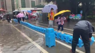 降雨致校门口积水，学校工作人员冒雨用凳子为学生搭“桥”