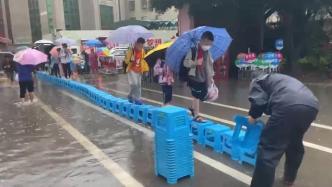 校门口积水，学校工作人员冒雨用凳子为学生搭“桥”