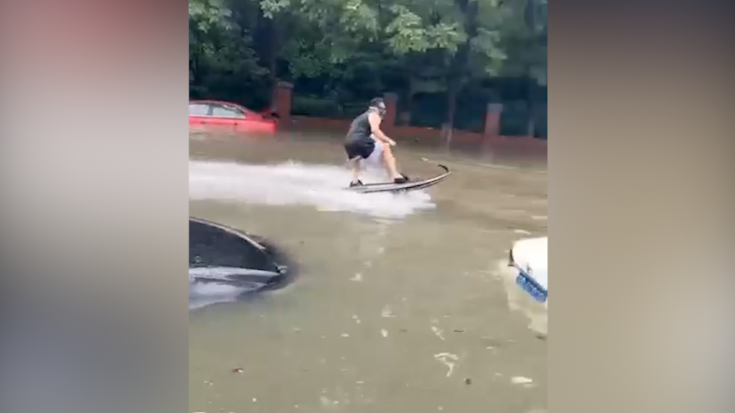 暴雨后道路积水成河，男子踩动力冲浪板出行：急着上班