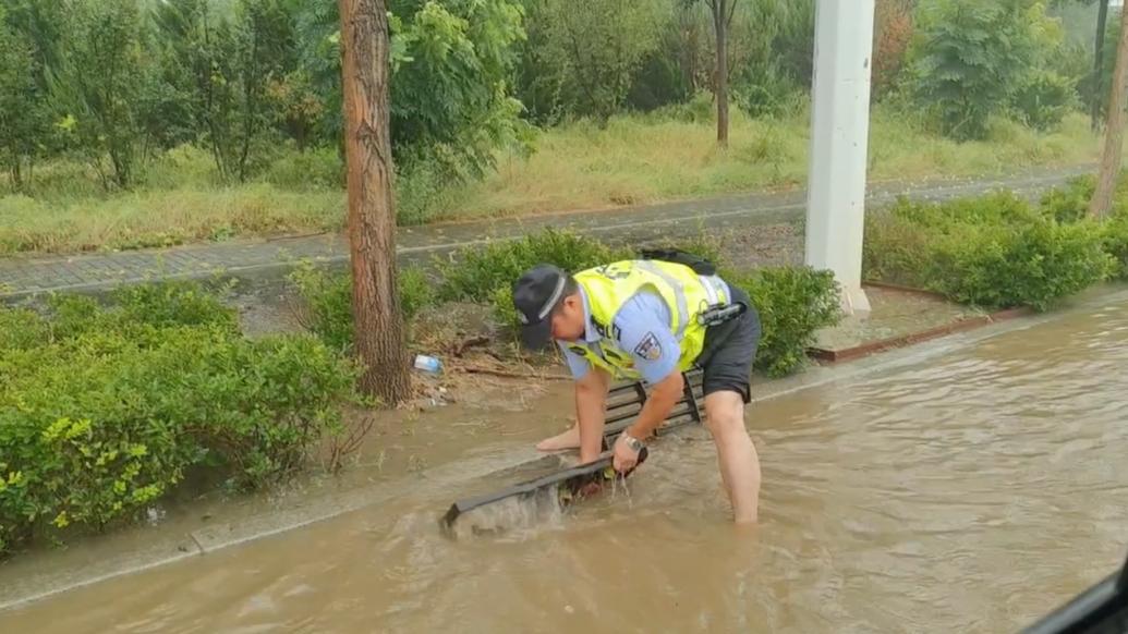 暴雨后道路积水严重，交警赤脚徒手清理排水井上方的垃圾