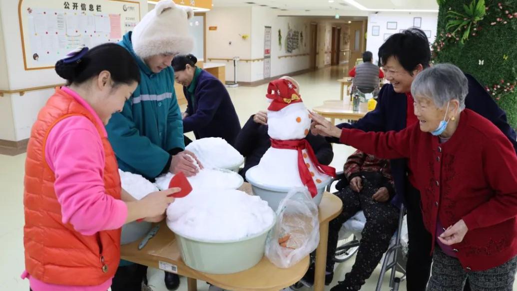 护理员搬雪进屋和老人玩堆雪人