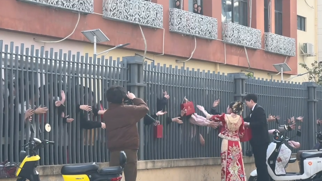 学生为学校附近结婚的新人送祝福，新郎拿来喜糖隔栅栏发放