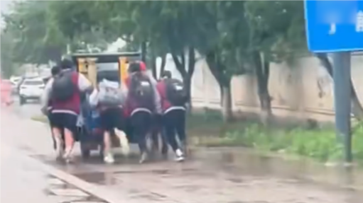 一群学生冒雨跑着帮三轮车大叔推车