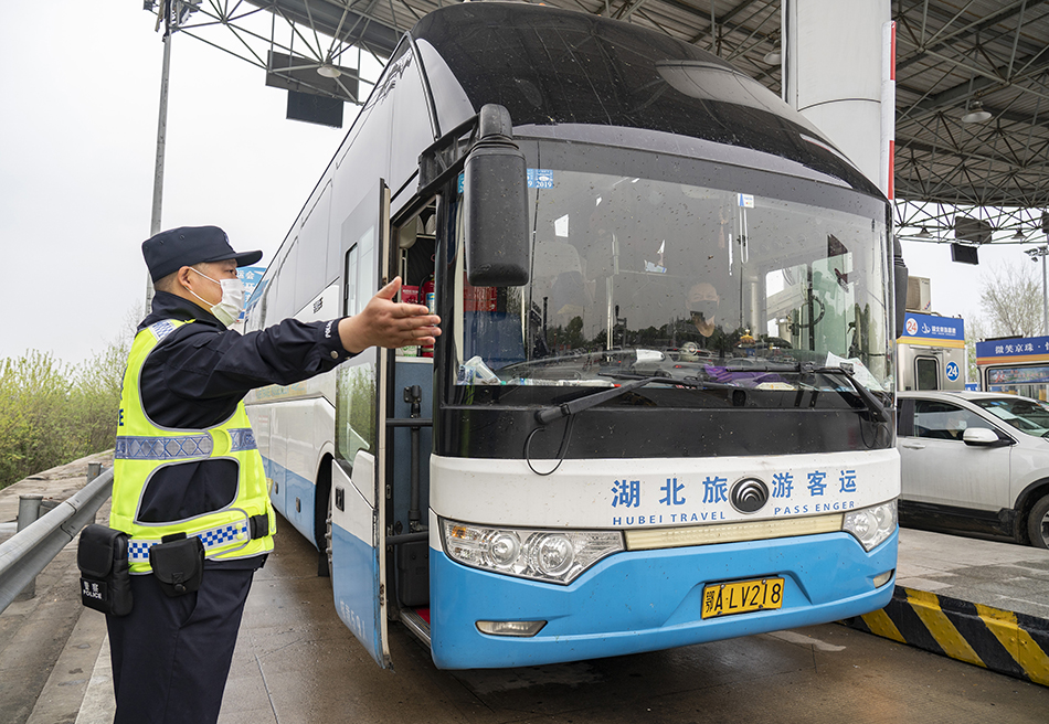 3月24日，在武汉西高速收费站交通卡点，执勤民警陈钢示意载有复工复产人员的大巴通行。