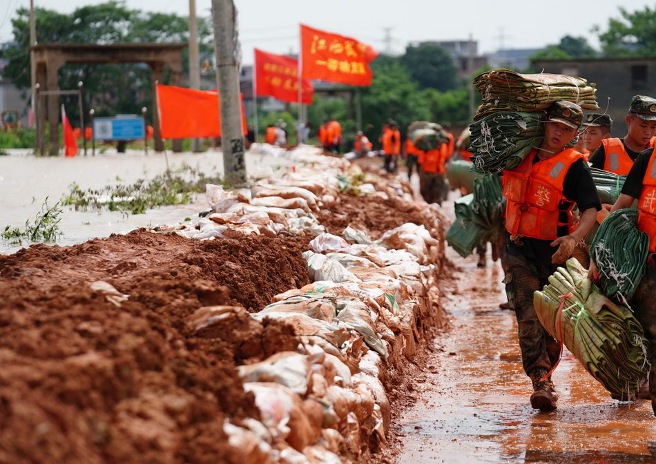 7月11日，武警战士在鄱阳县鄱阳镇江家岭村搬运编织袋，他们身旁的河水几乎要漫过防水墙上沿。