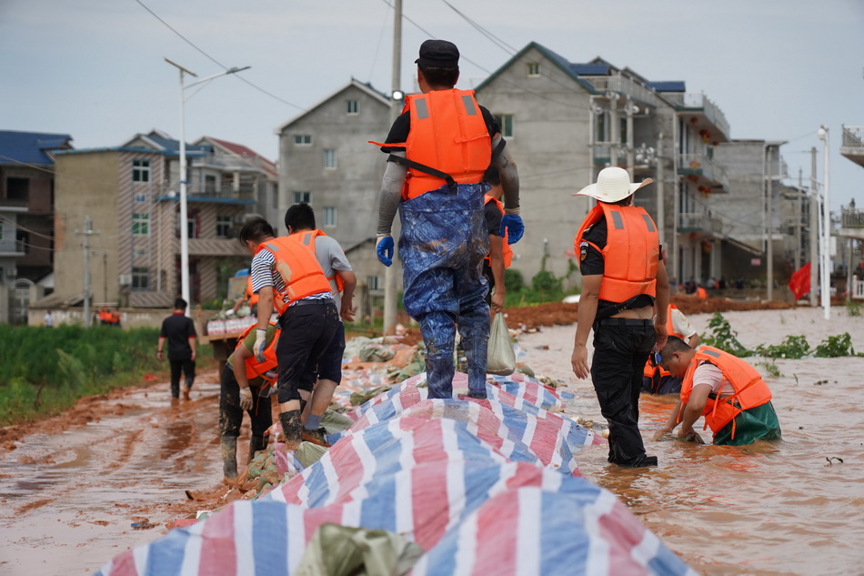 7月11日，在鄱阳县鄱阳镇江家岭村，来自鄱阳县城管局的党员干部在堤坝上给防水墙铺设防水布，防止河水侵蚀墙体。