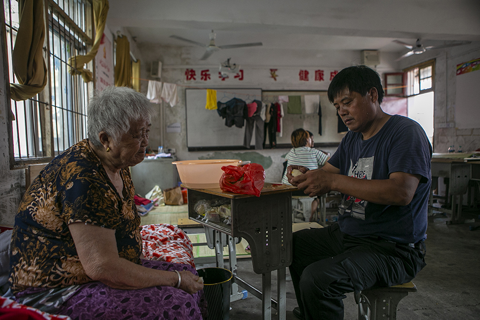 2020年7月16日，江西省鄱阳县五一中心学校安置点，桂湖村的黄和生在给母亲削梨，自从9号住进安置点已有七天，他今天特地出门买了水果回来给八十多岁的母亲吃。