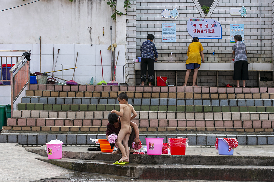 2020年7月16日，江西省鄱阳县五一中心学校安置点，家长在取水点外给孩子洗澡。