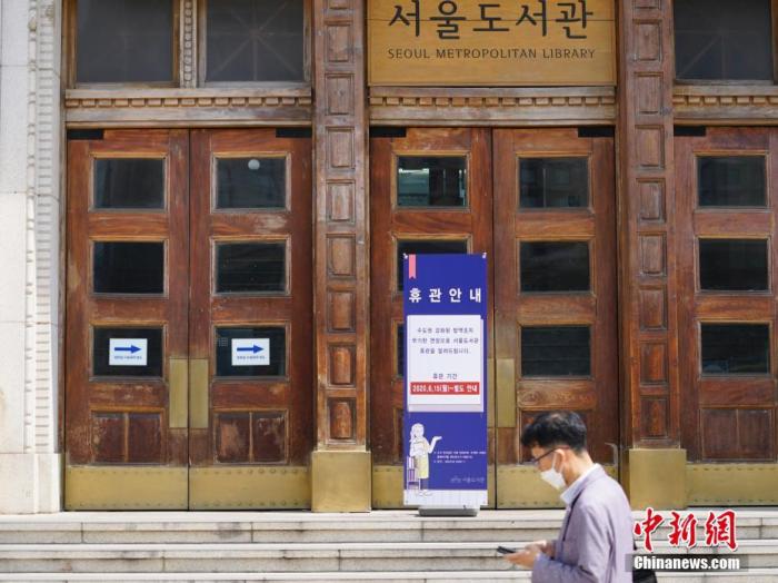资料图：2020年6月23日，一位韩国首尔市民经过首尔市立图书馆门前，该图书馆贴出闭馆通知。近来，包括韩国首尔、仁川、京畿道在内的首都圈确诊病例持续增加。 中新社记者 曾鼐 摄