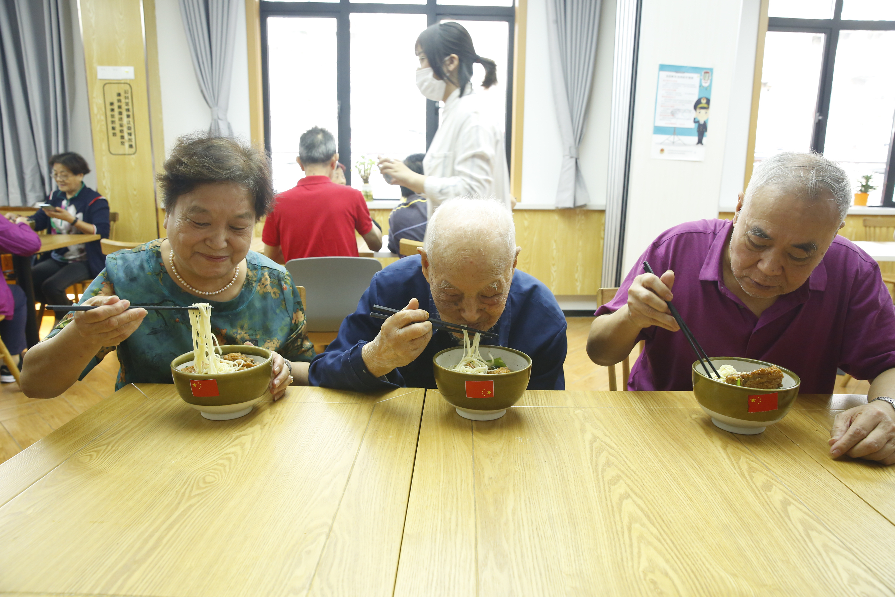 来自普陀区石泉路街道镇坪居民区106岁的李佩印老人（前排右二）正在和居民朋友一起吃国庆面。石泉路街道 供图
